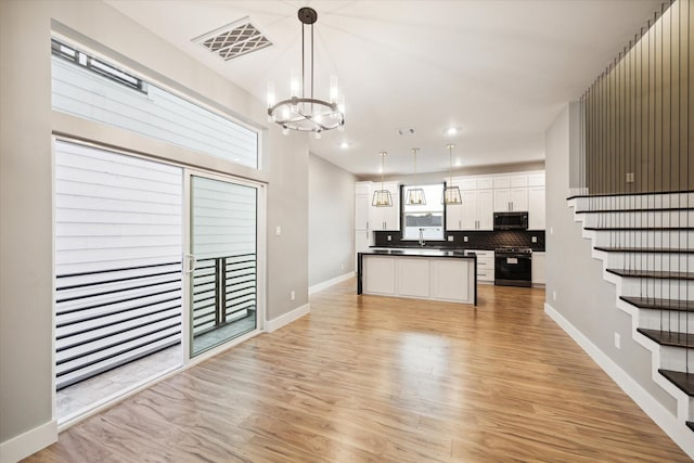 kitchen with stove, light wood finished floors, an inviting chandelier, visible vents, and dark countertops