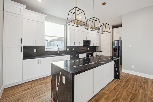 kitchen with a sink, stainless steel appliances, light wood finished floors, backsplash, and baseboards