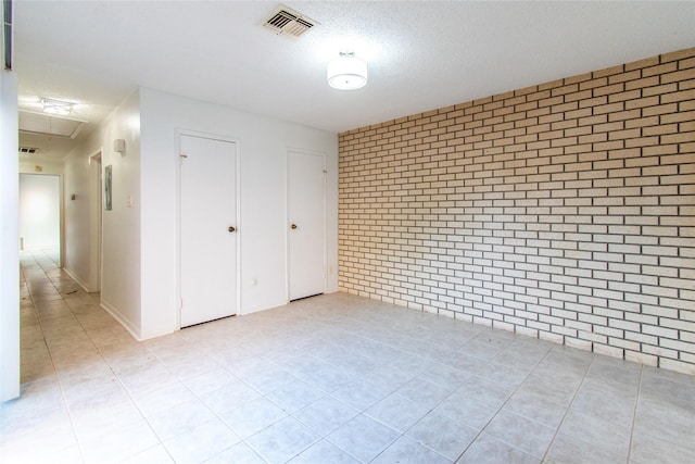2429 Briarwest Blvd, Houston, TX 77077 - unfurnished bedroom with light tile patterned floors, brick wall, attic access, and a textured ceiling