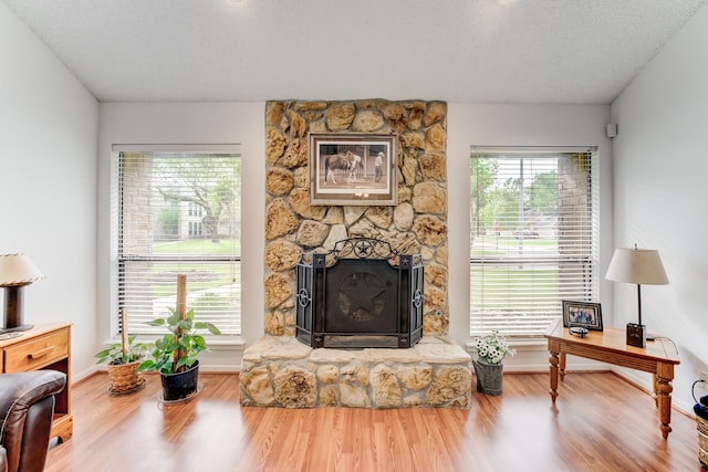 living room featuring a textured ceiling, baseboards, a stone fireplace, and wood finished floors