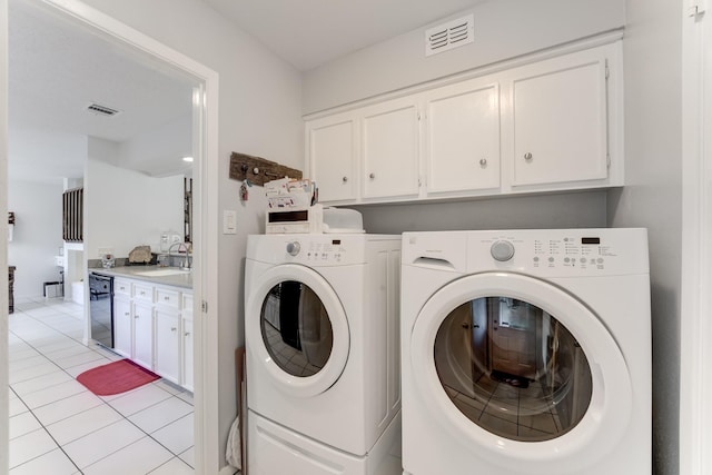 washroom featuring washer and dryer, light tile patterned flooring, visible vents, a sink, and cabinet space