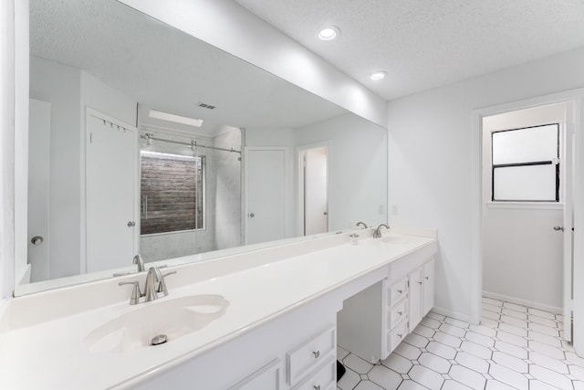 bathroom with a textured ceiling, visible vents, a sink, a shower stall, and double vanity