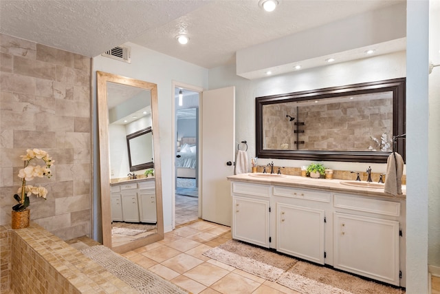 full bathroom featuring double vanity, a tile shower, a textured ceiling, tile patterned floors, and connected bathroom