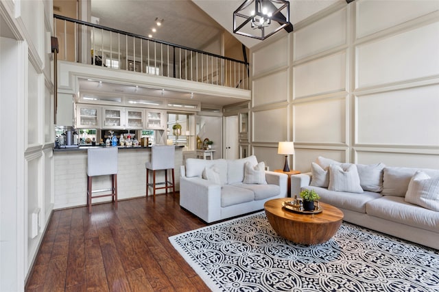 living room featuring a towering ceiling, dark wood-type flooring, a decorative wall, and a chandelier