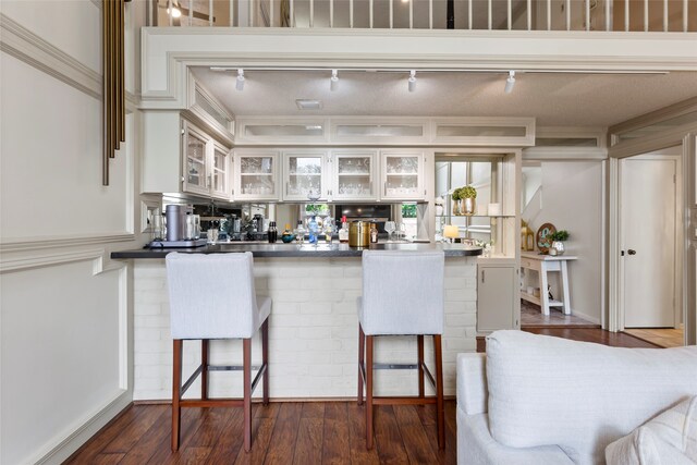 kitchen with a peninsula, dark countertops, glass insert cabinets, a kitchen bar, and dark wood finished floors