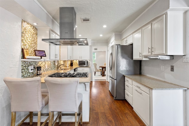 kitchen with island exhaust hood, stainless steel appliances, dark wood finished floors, backsplash, and light stone counters