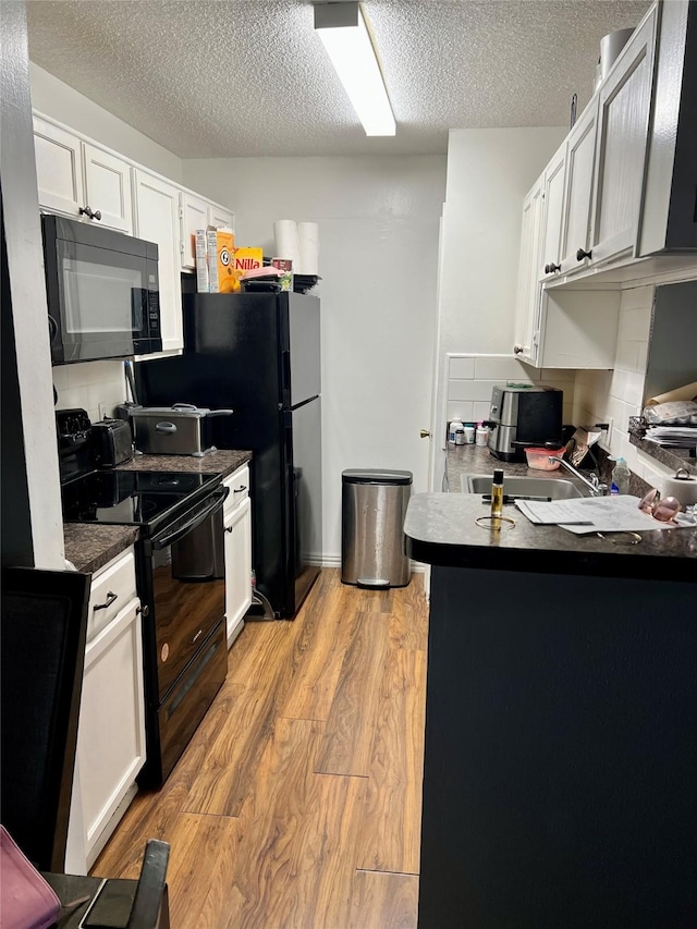 kitchen with a textured ceiling, black appliances, white cabinetry, dark countertops, and light wood-style floors