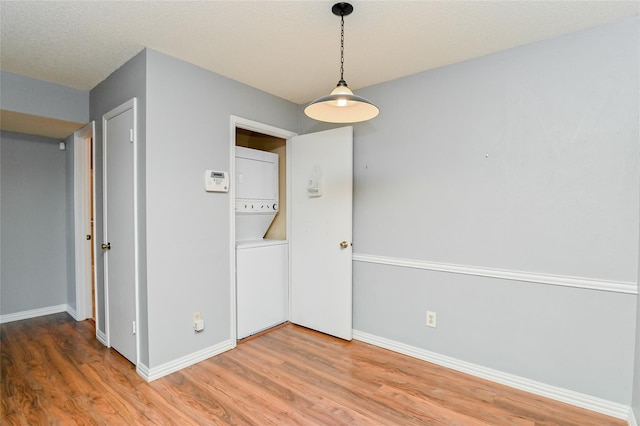 unfurnished room featuring stacked washer / dryer, baseboards, and light wood-style floors