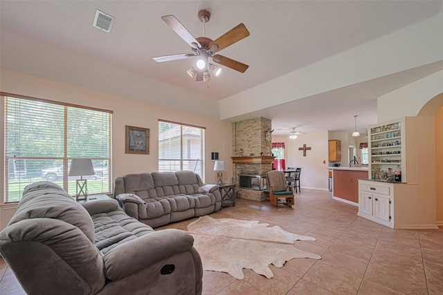 living area featuring ceiling fan, light tile patterned flooring, baseboards, a stone fireplace, and bar