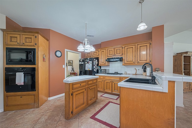kitchen with black appliances, tile counters, under cabinet range hood, a chandelier, and a peninsula