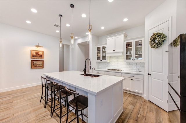 20447 Avelignese Way, Tomball, TX 77377 - kitchen with a sink, stainless steel gas cooktop, a breakfast bar area, light wood finished floors, and decorative backsplash
