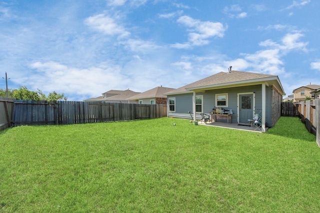 rear view of property featuring a yard, a patio, a shingled roof, and a fenced backyard