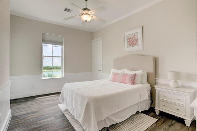 bedroom featuring a wainscoted wall, crown molding, visible vents, and dark wood-style floors