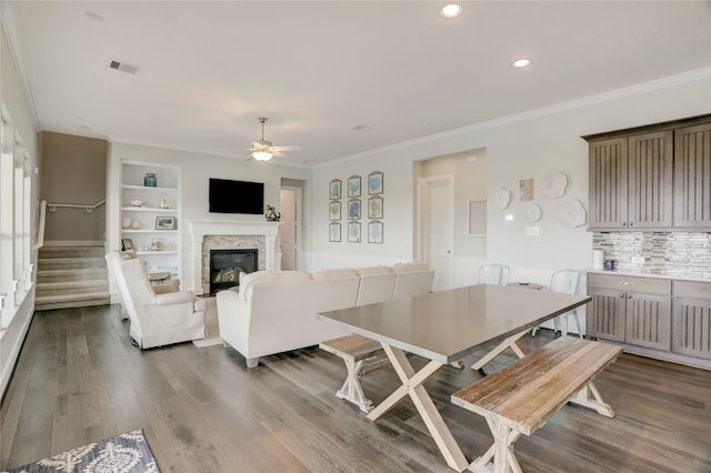 dining space featuring a ceiling fan, a glass covered fireplace, visible vents, built in features, and dark wood-style floors