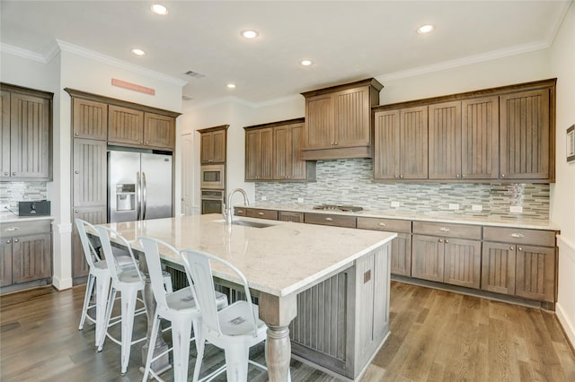 kitchen featuring a kitchen bar, an island with sink, a sink, backsplash, and appliances with stainless steel finishes