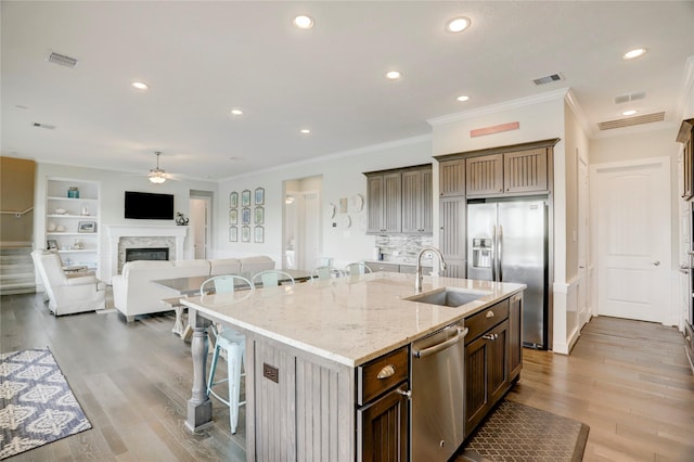 kitchen with a ceiling fan, an island with sink, a breakfast bar, a sink, and appliances with stainless steel finishes