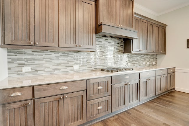 kitchen featuring tasteful backsplash, stainless steel gas stovetop, light wood-type flooring, light stone counters, and crown molding