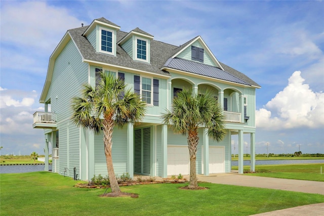 raised beach house with an attached garage, a water view, a shingled roof, concrete driveway, and a front lawn
