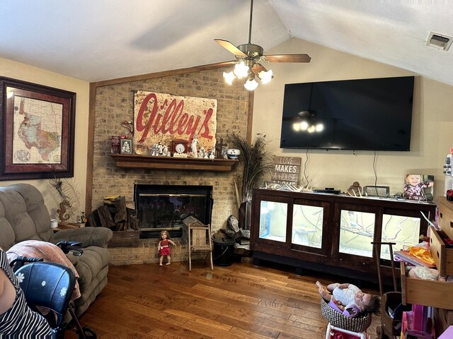 living area with vaulted ceiling, hardwood / wood-style flooring, ceiling fan, and a brick fireplace