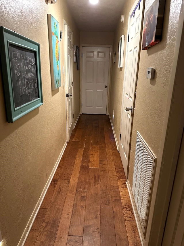 hall featuring dark wood-style flooring, a textured wall, and baseboards