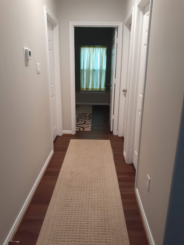 corridor with dark wood-type flooring and baseboards