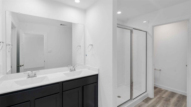 full bathroom featuring double vanity, wood finished floors, a stall shower, and a sink