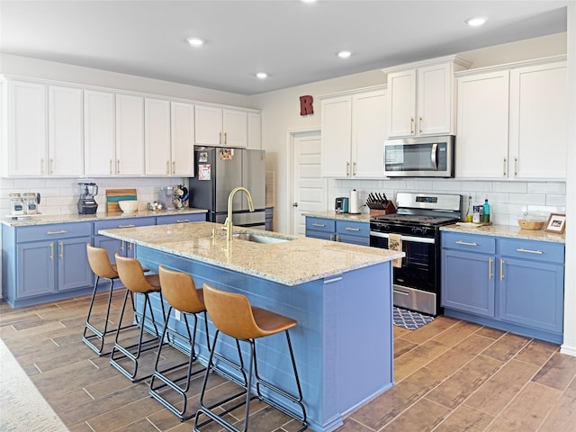 kitchen with backsplash, appliances with stainless steel finishes, blue cabinetry, and a sink
