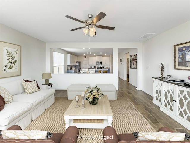 living room with visible vents, wood finished floors, baseboards, and ceiling fan