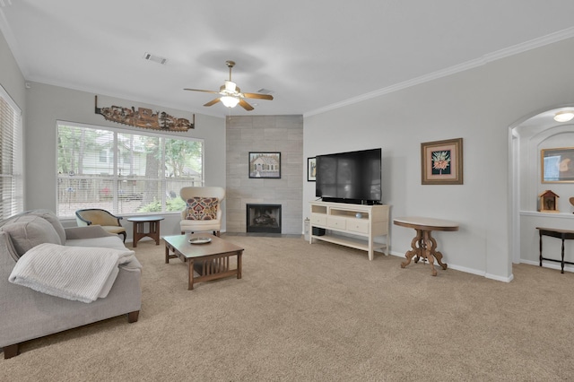 carpeted living area featuring ceiling fan, baseboards, arched walkways, ornamental molding, and a tile fireplace