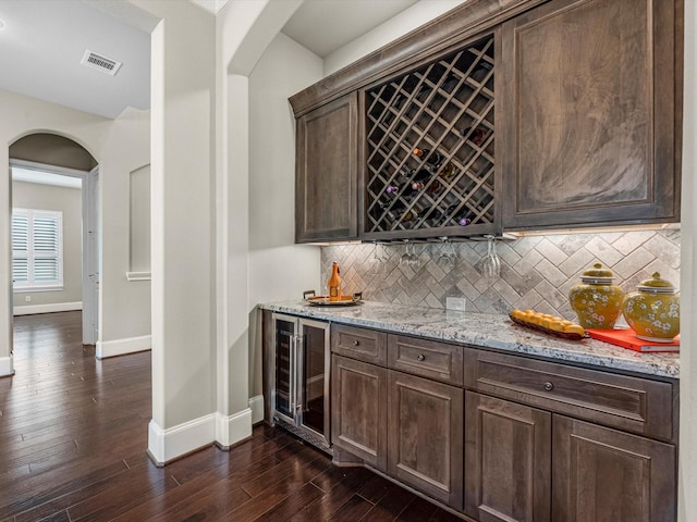 bar with wine cooler, a dry bar, baseboards, visible vents, and arched walkways