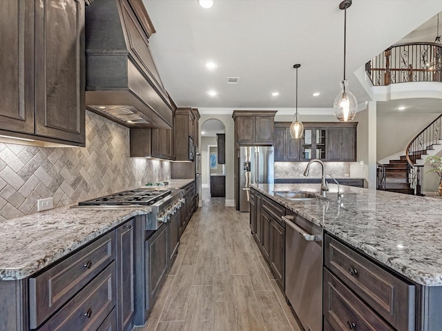 kitchen with custom exhaust hood, a sink, dark brown cabinetry, arched walkways, and stainless steel appliances