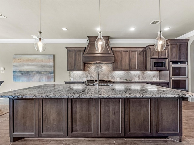 kitchen with crown molding, visible vents, a large island with sink, appliances with stainless steel finishes, and custom range hood