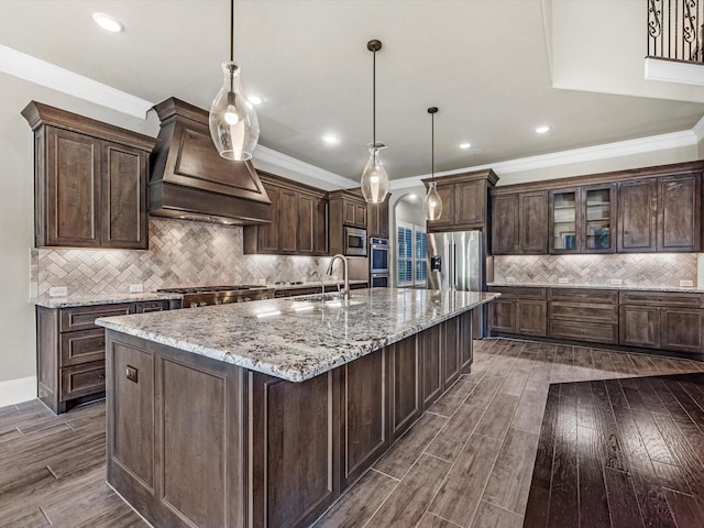 kitchen with a sink, custom exhaust hood, dark wood-style flooring, backsplash, and appliances with stainless steel finishes