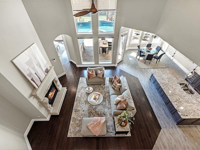 living room featuring wood finished floors, a ceiling fan, a high ceiling, arched walkways, and a glass covered fireplace