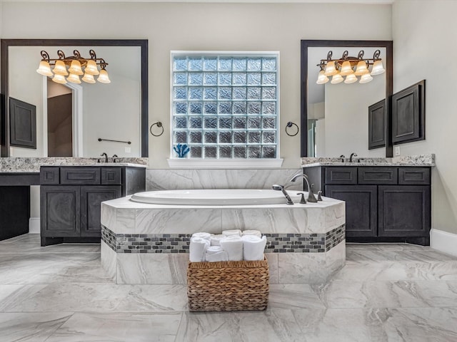 bathroom featuring marble finish floor, a sink, two vanities, and a bath