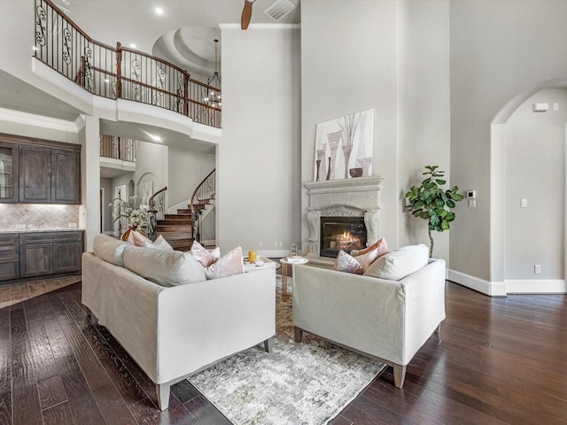 living area with stairs, a towering ceiling, dark wood finished floors, arched walkways, and a premium fireplace