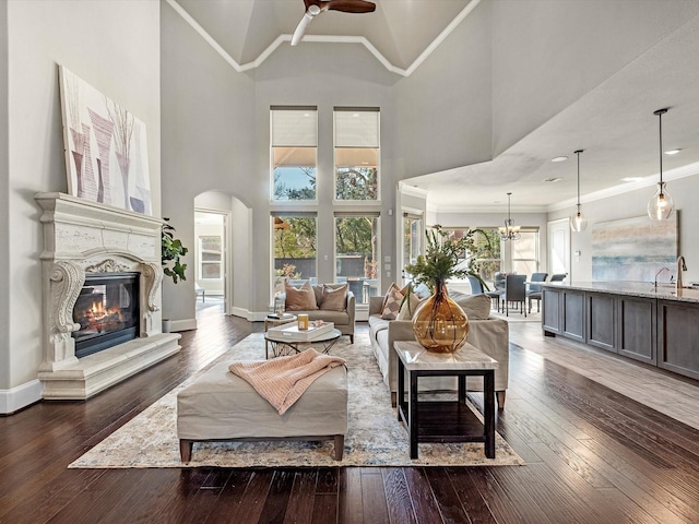 living room with a glass covered fireplace, ceiling fan with notable chandelier, hardwood / wood-style floors, and arched walkways