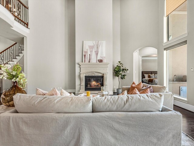 living area with dark wood finished floors, stairway, arched walkways, a premium fireplace, and a high ceiling