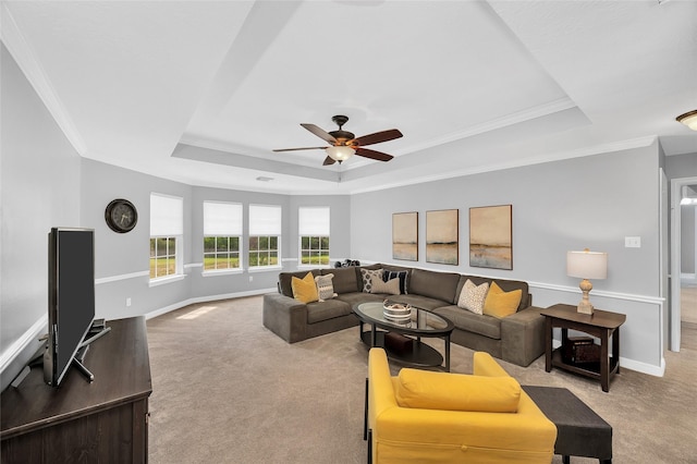 living area featuring a raised ceiling, carpet floors, ceiling fan, baseboards, and crown molding