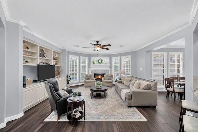 living area featuring a ceiling fan, crown molding, dark wood-type flooring, and a lit fireplace