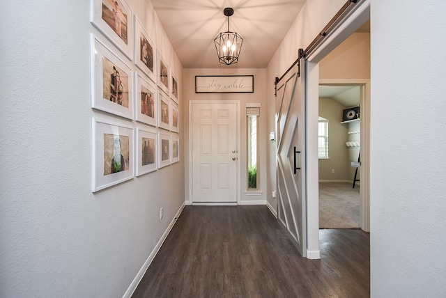 entryway with a barn door, dark wood finished floors, baseboards, and a notable chandelier