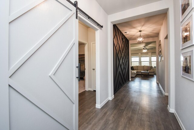 hall featuring baseboards, a barn door, and dark wood-style floors