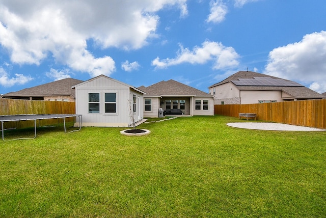 rear view of property featuring a trampoline, a patio area, a lawn, and a fenced backyard