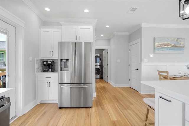 kitchen with light wood finished floors, stacked washing maching and dryer, light countertops, white cabinets, and appliances with stainless steel finishes