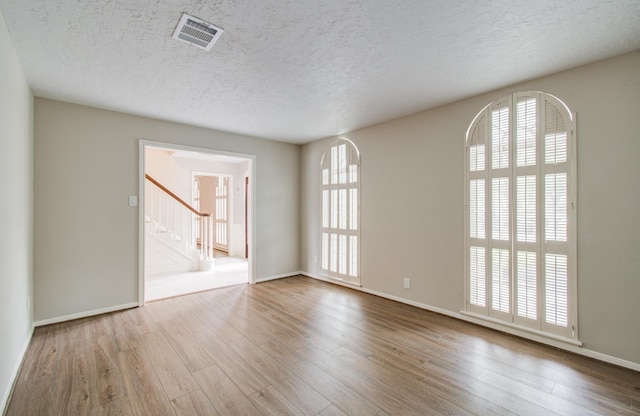 11022 Riverview Dr, Houston, TX 77042 - spare room featuring a textured ceiling, baseboards, visible vents, stairs, and wood finished floors