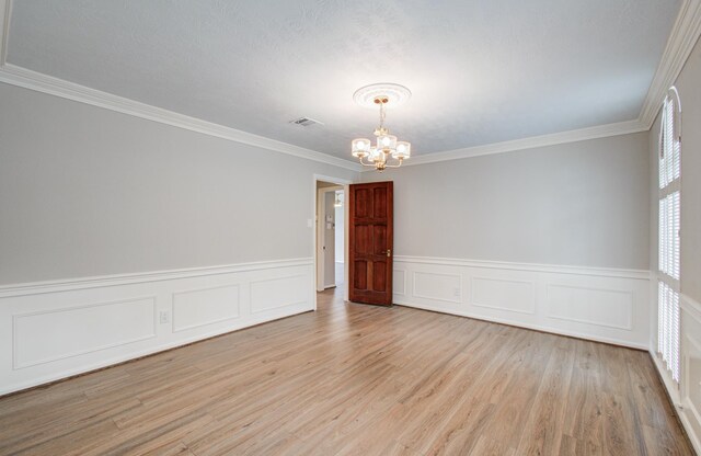 11022 Riverview Dr, Houston, TX 77042 - empty room with ornamental molding, an inviting chandelier, visible vents, a wainscoted wall, and light wood-type flooring