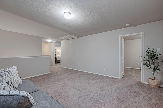 unfurnished room with a textured ceiling, attic access, baseboards, and carpet