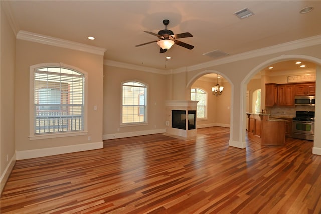 unfurnished living room featuring baseboards, visible vents, ceiling fan with notable chandelier, wood finished floors, and arched walkways