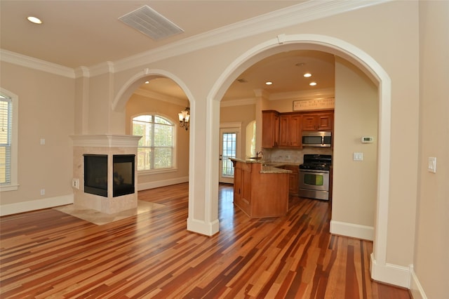 unfurnished living room with wood finished floors, a fireplace, visible vents, baseboards, and ornamental molding