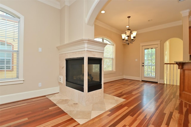unfurnished living room with a tile fireplace, an inviting chandelier, plenty of natural light, and wood finished floors